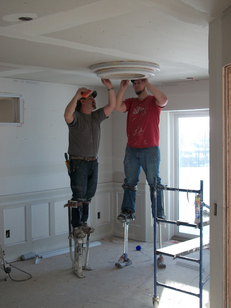 Scott and Kyle, one of his 'henchmen', glue and staple the "baby" corner bead in place on their stilts.