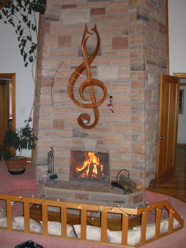 The mantle was a stylized treble clef rendered in NZ totara, 24k gold plated 1/8€ high carbon barstock, Sri Lankan ebony, mother of pearl [MOP] and snow flake obsidian cabochons. There was a fluorescent lamp carved into the backside for accent and all electrical wiring was through the stonework.